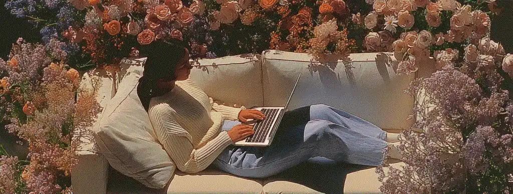 Person in white sweater working on laptop surrounded by flowers